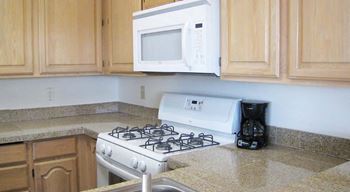 Kitchen with upper and lower cabinets, and white microwave and oven with stove cooktop.